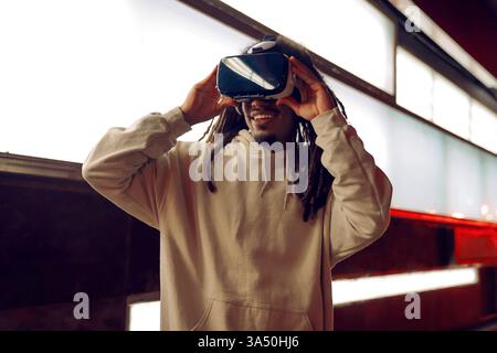 Young happy African American man wearing VR headset in a modern room with glowing lamps. A technology and innovation themed image suited for VR, gaming, and digital experiences. Stock Photo