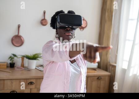 Vibrant portrait of an African woman in pink, enjoying a virtual reality headset. This indoor lifestyle image highlights wearable technology and the excitement of immersive experiences. Ideal for campaigns about virtual reality, gadgets, digital wellbeing, and home entertainment. Stock Photo