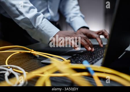 Hands of a Black male network engineer typing on a laptop in a server room. A focused IT and data center scene highlighting networking, maintenance and cybersecurity. Suitable for technology careers, IT professionals and enterprise infrastructure topics. Stock Photo