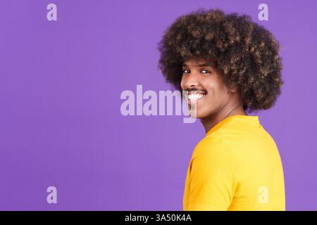 Happy African man with curly hair smiles at the camera in a studio setting. Ideal for lifestyle, confidence and positive emotion branding. Stock Photo