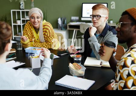 Portrait of a creative young man collaborating with a diverse design team during a business meeting and enjoying snacks. This scene highlights teamwork and a relaxed office culture. Great for features on innovation and collaborative work. Stock Photo