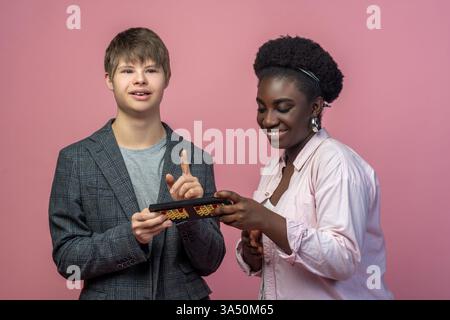 Joyful scene of a young man with Down syndrome pointing up while an African American woman smiles and holds an abacus. A positive depiction of learning, inclusion, and teamwork ideal for education and disability awareness campaigns. Great for inclusive branding and social impact storytelling. Stock Photo