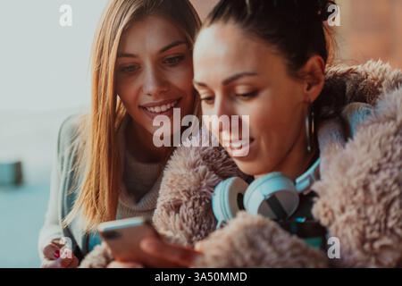 Two friends at a university campus share a light moment while checking a smartphone. This image highlights student life, friendship, and mobile communication. Stock Photo