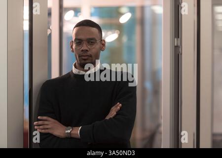 African American man looking at camera in a modern office lobby. This diverse professional portrait supports corporate branding, leadership and workplace communication visuals. Stock Photo