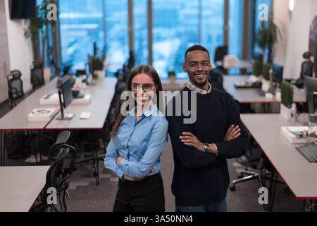Two diverse professionals, a woman and an African American man, pose in a modern office lobby. This upbeat corporate image supports teamwork, diversity, and professional workplace visuals. Stock Photo