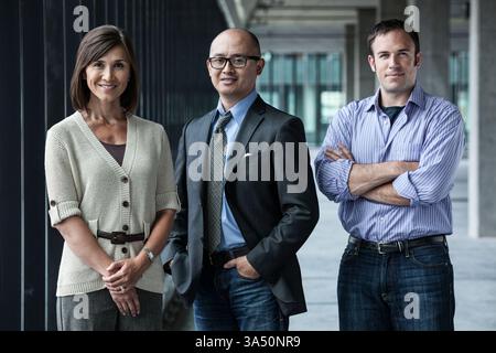 Diverse group in an open plan office space with an Asian American woman standing with two colleagues. The modern, collaborative scene suits business, teamwork and workplace campaigns. Stock Photo
