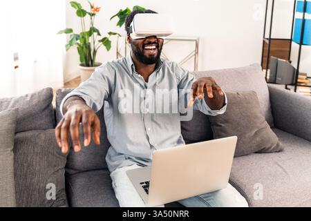 Handsome Black man at home playing with a virtual reality headset. Relaxed living room setting under a tech-forward lifestyle vibe. Perfect for gaming, tech, and home entertainment campaigns. Stock Photo