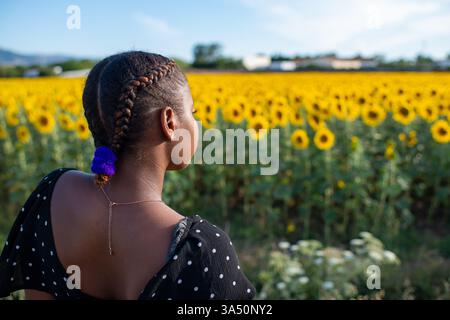 Young African American female standing on blossoming sunflowers in field Stock Photo