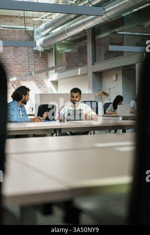 Diverse group of professionals collaborating on a project in a modern office. Hispanic and Indian colleagues share ideas during a meeting, highlighting teamwork and strategic planning in a corporate setting. Stock Photo