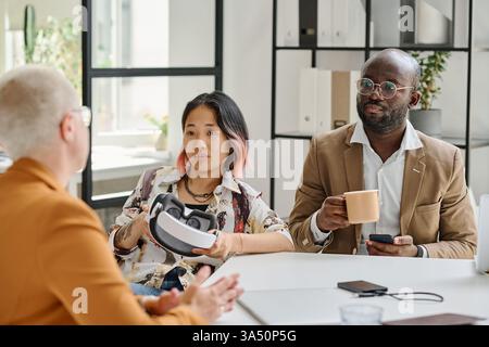 Group of diverse developers test virtual reality glasses around a table in a modern meeting. This scene is ideal for technology, software, and innovation themes. Stock Photo