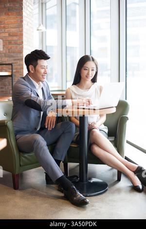 Smiling Chinese professionals collaborate on a laptop at a cafe table. The casual business setting highlights teamwork, connectivity, and productive meetings outside the office. Ideal for content about flexible work, client meetings, and urban collaboration. Stock Photo