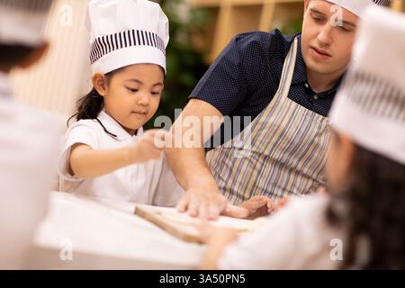 Chinese children learning how to cook with caucasian male teacher in school Stock Photo