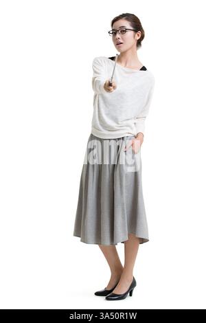 Studio portrait of a Chinese female teacher in glasses, standing against a white background. She points a forward-facing pointer while keeping hands in her pockets, conveying confidence and professionalism. A clear image for education, training, and classroom or corporate presentation contexts, with strong copy space. Stock Photo
