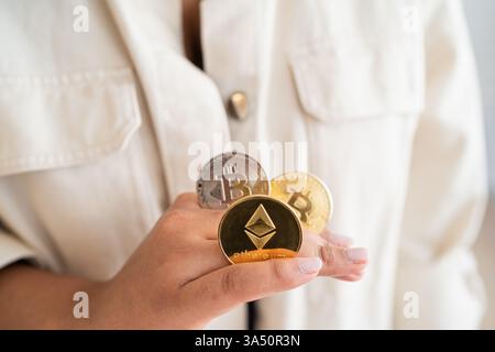Black woman with cryptocurrency coins between fingers standing at home. A modern finance concept ideal for topics on crypto, digital currency, and investment. Stock Photo
