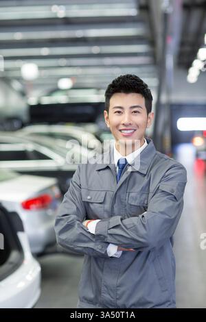 Male Chinese auto mechanic in a repair shop with a confident, professional presence. Demonstrates expertise in the automobile industry with a focus on car maintenance and repair services. Suitable for automotive service, garage, and dealership imagery featuring a skilled technician. Stock Photo