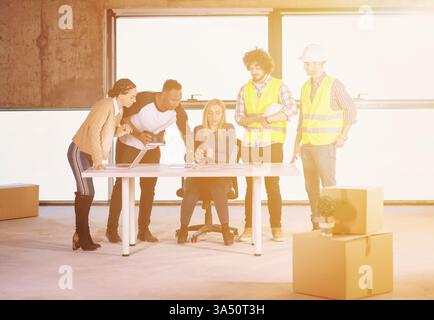 A young, multiethnic business team on a construction site checks documents and workflow using a VR headset and laptop. The image conveys collaboration, innovation, and fieldwork technology. Perfect for topics on construction, business technology, and diverse teams. Stock Photo