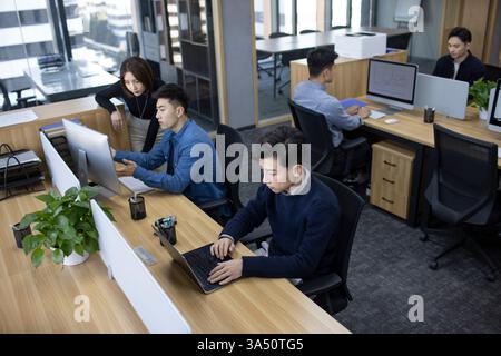 Chinese IT experts collaborating at their laptops in an office setting. This scene suits tech teams, software development and collaborative IT projects. Stock Photo