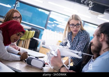 Diverse group of professionals collaborating at a table with gadgets and documents, discussing drone technology and VR glasses for business advancement. Ideal for technology, startup, and teamwork visuals. Suitable for corporate reports, brainstorming, and innovation campaigns. Stock Photo