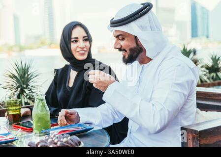Happy couple in Dubai enjoying time at a cafe. The man and woman wear traditional attire, sharing a warm conversation. Ideal for features on couples lifestyle, travel in the Middle East, and cafe culture. Stock Photo