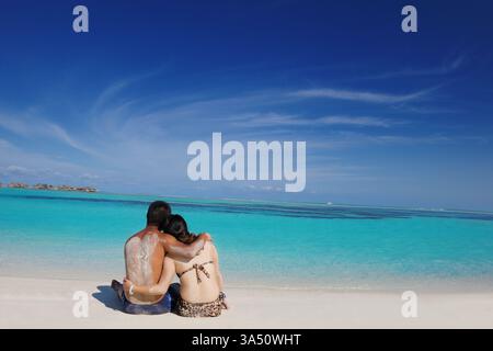 A happy young Asian couple enjoys a romantic summer day on a white sandy beach in the Maldives. This scene suits travel, romance, and getaway campaigns. Perfect for seaside holidays, beach photography, and couple lifestyle promotions. Stock Photo