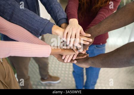 From above view of a diverse group stacking hands in a sign of teamwork and solidarity. Ideal for diversity, inclusion and corporate communications about collaboration and unity. Great for business and teamwork campaigns. Stock Photo