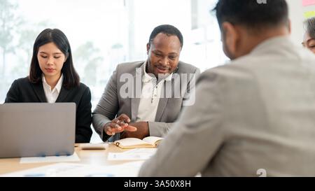 An African American businessman and an Asian secretary join a diverse finance team for an investment planning session. They discuss ideas and share insights in a corporate boardroom setting. Ideal for marketing materials about leadership, teamwork, and multicultural collaboration in business. Stock Photo