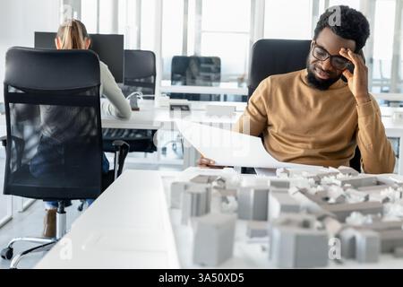 Dark-skinned young architect working in an office, looking tired. This scene reflects the demanding nature of creative professions and office stress. Stock Photo