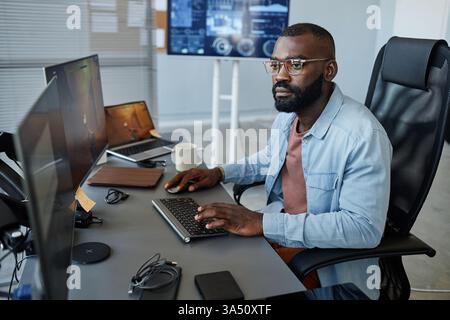 Portrait of a Black game developer focused on level design at a computer in an office. The scene highlights tech careers, software development, and the gaming industry. Stock Photo