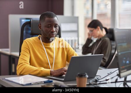 Portrait of a young Black software developer working on a laptop in an indoor office setting. Ideal for IT, programming, software development, cybersecurity, and data analytics topics. The composition provides clear copy space for overlay text. Stock Photo