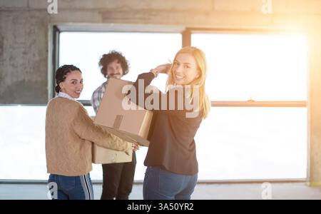 Happy young team in a startup office moves boxes during relocation, with sunlight streaming through the windows. This energetic office scene conveys teamwork, growth, and a dynamic corporate culture. Suitable for entrepreneurship, office move announcements, and startup branding. Stock Photo