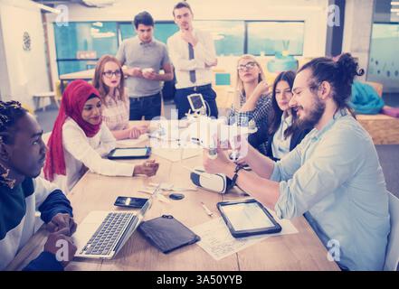 Smiling mixed race man with a beard collaborates on drone technology with diverse colleagues around a table. They wear VR glasses in a modern office, suggesting team brainstorming and tech focus. Ideal for business, technology, and team meeting visuals. Stock Photo