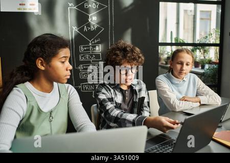 Group of diverse children discusses software on a computer during an IT lesson. The desk scene showcases teamwork, digital literacy, and classroom technology. Stock Photo