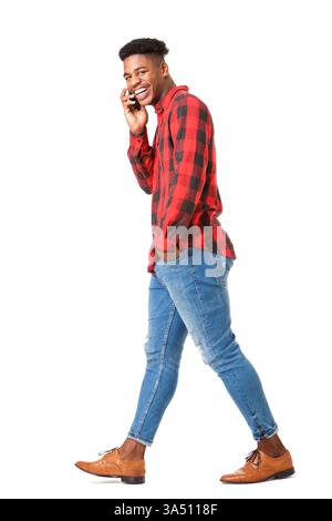 Smiling Black man in a casual outfit talks on his cellphone while walking. Set against a clean white backdrop, the image provides generous copy space for text. Ideal for lifestyle, mobile technology, and fashion campaigns highlighting everyday connectivity. Stock Photo