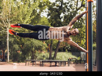 Fit man performs push-ups on parallel bars outdoors, showcasing upper body strength and athletic conditioning. This dynamic fitness shot suits gym ads, outdoor training, and sport lifestyle campaigns. Stock Photo