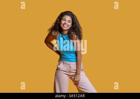 Smiling African American woman stands with one hand on her hip against a bright yellow backdrop. This studio shot works well for fashion, lifestyle branding, and positive-ambition campaigns. Stock Photo