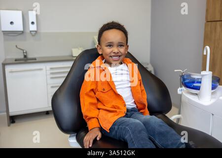 Dark-skinned boy looks happy after a dentist session in a pediatric dentistry setting. A kid-friendly healthcare image that promotes dental care and healthy smiles. Great for healthcare, dentistry, and children's health topics. Stock Photo