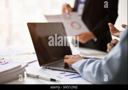 Business people working together on a laptop at a table in a bright office. A diverse group collaborates, brainstorms and shares ideas in a professional team setting. Stock Photo