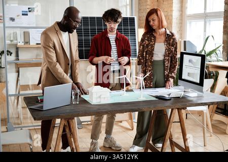 A diverse group of engineers collaborate at a table in the office, discussing a project. The scene showcases teamwork and innovation in a professional setting. Suitable for technology, design, business, and corporate communications. Stock Photo