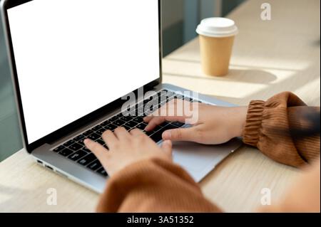 Close-up of a woman using a laptop in a cafe, featuring a white-screen laptop mockup. The shot conveys freelance, remote working, or student themes with a contemporary workspace vibe. Great for tech, internet, and digital productivity contexts. Stock Photo