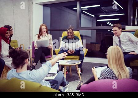 A cheerful, diverse startup team collaborates in a modern office, using laptops and a tablet to brainstorm ideas. The image highlights teamwork, innovation, and a positive workplace vibe. Ideal for features on entrepreneurship, collaboration, and business growth. Stock Photo