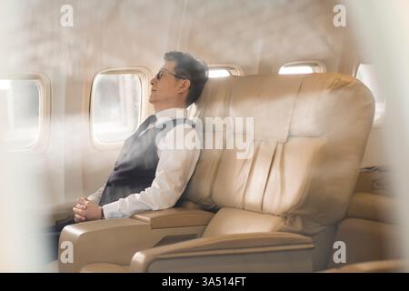 Chinese businessman in glasses sleeping with hands together on an airplane seat. Travel and business lifestyle image for in flight relaxation and corporate travel themes. Stock Photo