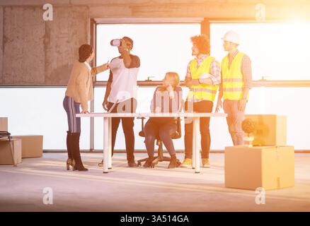 Young multiethnic business team checking documents and workflow on a construction site using a virtual reality headset and laptop. Ideal for technology, construction, collaboration, and virtual reality in field operations visuals. Stock Photo