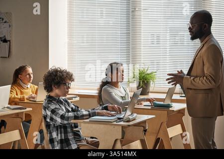 African American teacher guiding a group of children through a computer activity. The classroom scene captures inclusive education, technology in learning, and collaborative problem solving. Useful for education, STEM, and diversity messaging. Stock Photo
