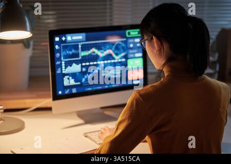 Rear view of a young computer engineer working late at the office, developing new software. This tech-focused image highlights programming, software development, and women in tech. Stock Photo