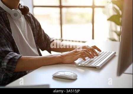 Close-up of a male programmer in a flannel shirt typing at his computer. The shot highlights coding and project work as he responds to emails, making it suitable for technology and software development contexts. Ideal for modern office or home office branding. Stock Photo