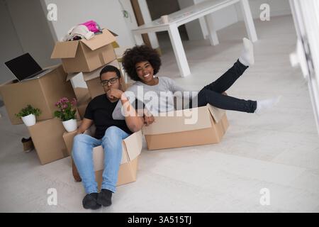 African American couple sits inside a box filled with packing material, having fun after moving into a new home. Playful, lifestyle moment that communicates relocation, home life, and togetherness. Stock Photo