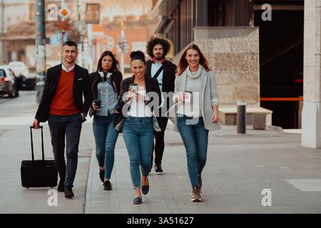 Diverse group of young businesspeople on a coffee break, drinking coffee to go and using smartphones. This dynamic scene conveys teamwork, urban culture, and tech-friendly collaboration for business and startup themes. Stock Photo