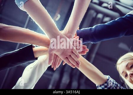 Diverse group of business people put their hands together in celebration in the office. This positive teamwork image conveys success, collaboration and shared achievement. Stock Photo