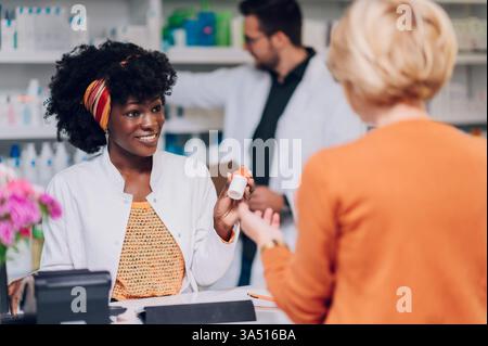 Young African American woman pharmacist discusses medications with a senior customer inside a pharmacy. The scene emphasizes healthcare, patient support, and pharmaceutical expertise. Suitable for pharmacy services, community health, and retail healthcare campaigns. Stock Photo