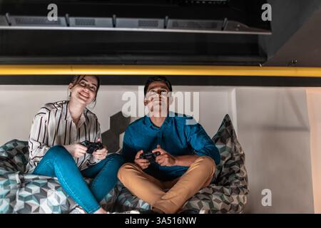 Casual startup office scene with colleagues playing computer games during a break. A diverse team competes in a relaxed, modern workspace, highlighting teamwork and creativity. Stock Photo